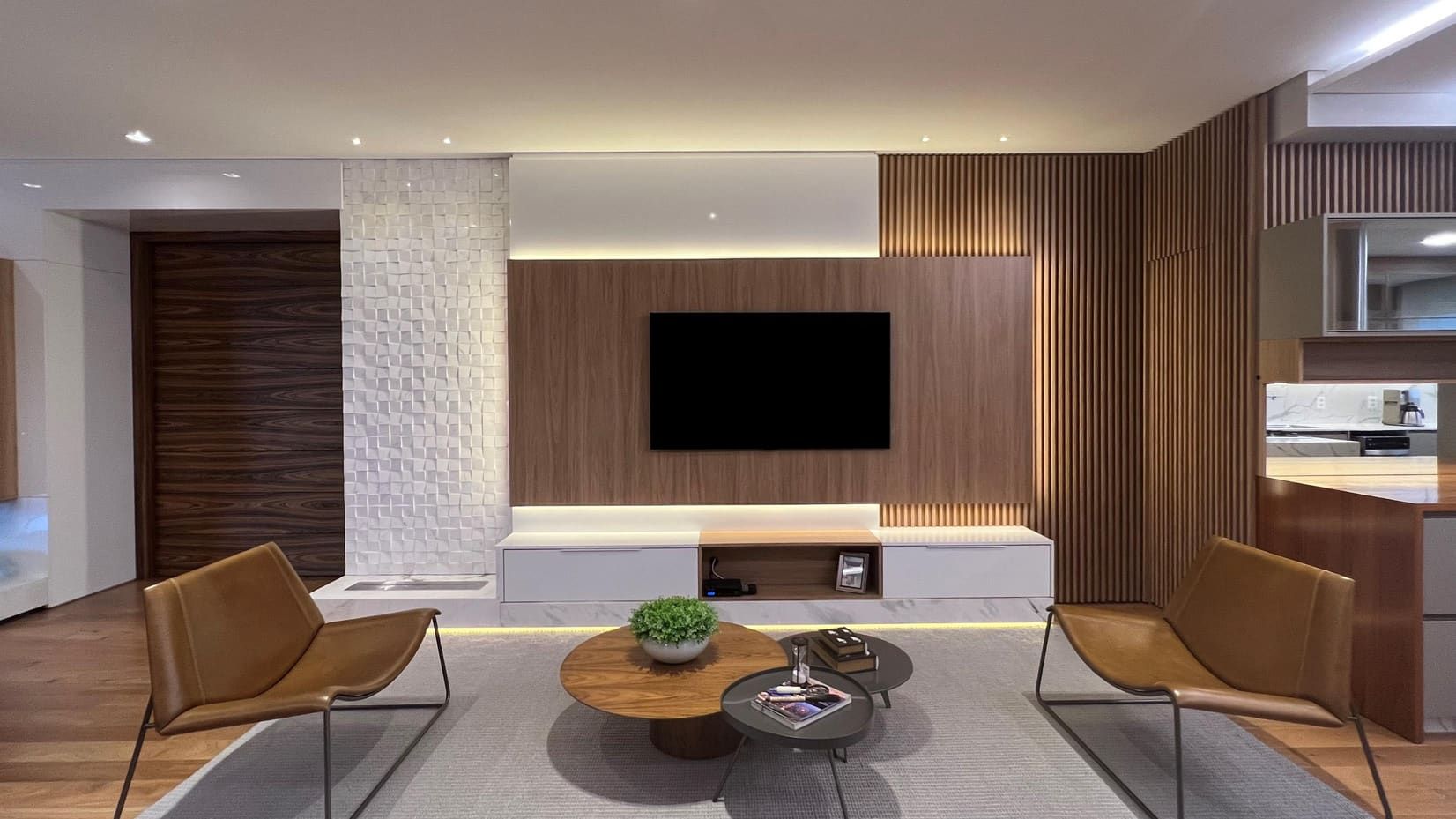 Living room with a slatted walnut media wall, a sculpted stone column and leather lounge chairs